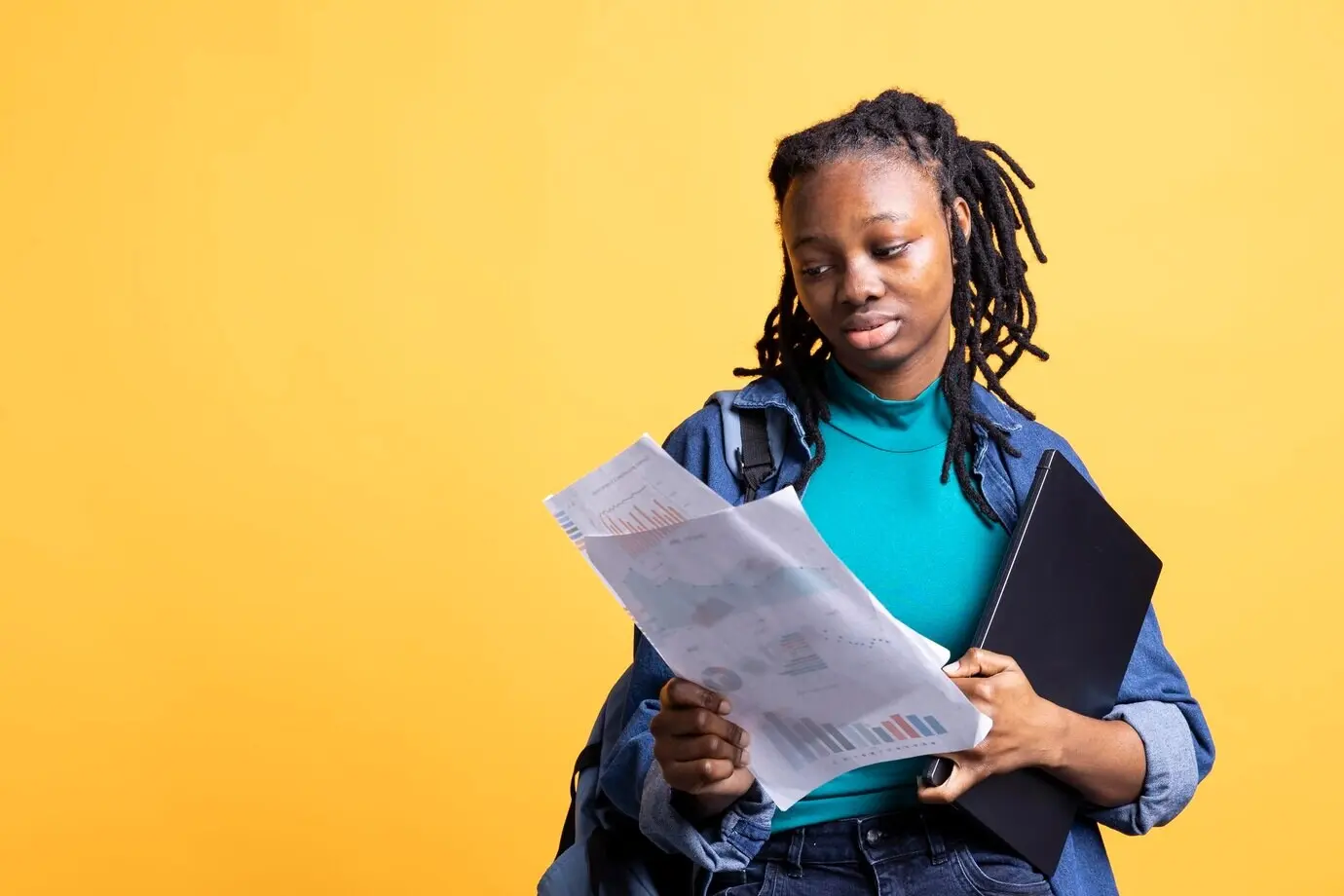Jeune fille lisant des documents contenant des graphiques économiques, sur fond de studio.